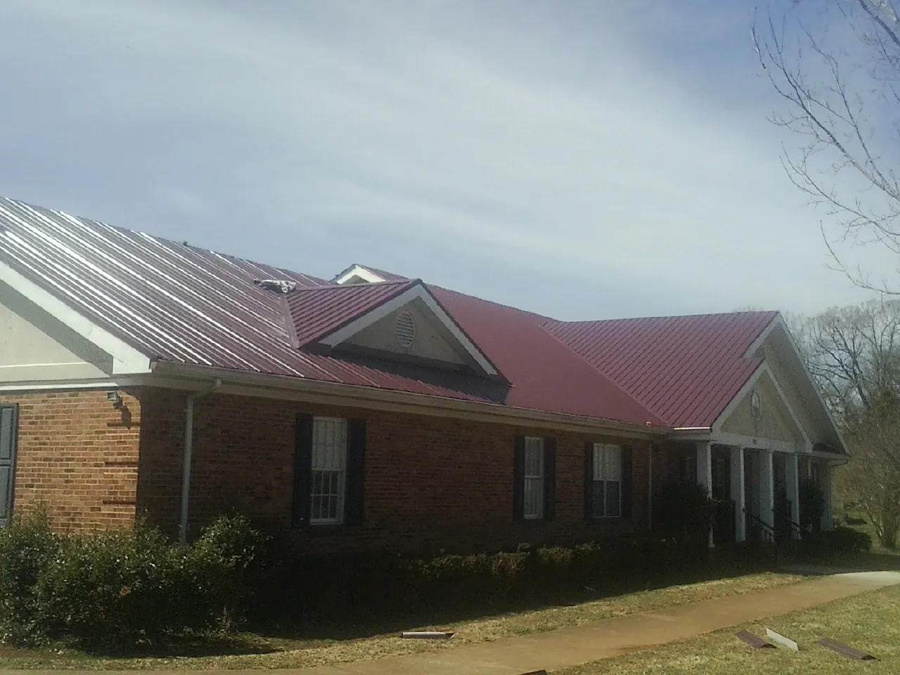 Red metal roof with gabled entries on a long brick building, from a Hail Damage Roof Repair job in Bloomington